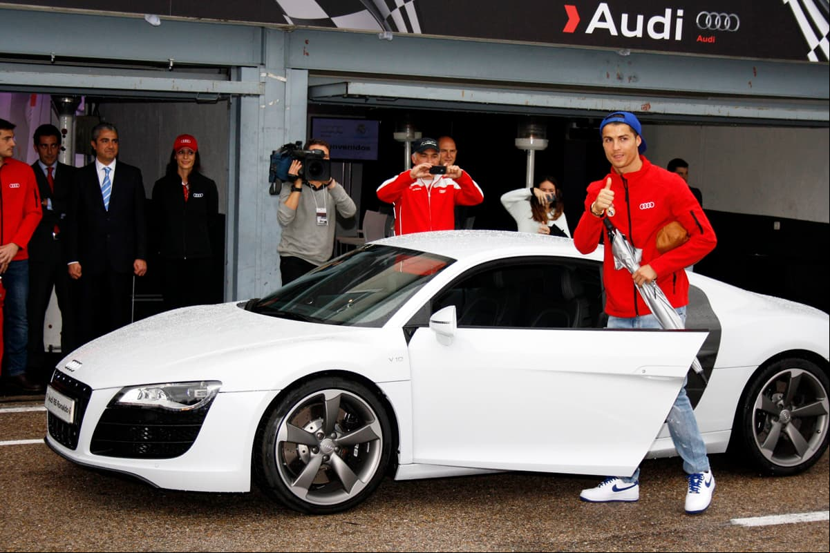 En esta imagen vemos a Ronaldo en 2012, cuando Audi le entregó las llaves de un R8 Coupé 5.2 FSI quattro R tronic que, con su carrocería blanca, hizo honor al color que distingue al Real Madrid, club español en el cual aún se desempeña el lusitano. La marca alemana patrocina a esta institución desde 2003. Desde el año 2006 Audi también es patrocinador de su gran rival en la Liga Española: el Barcelona, donde juega Lionel Messi.